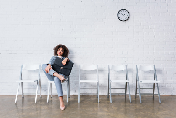 Ontspannen en verveelde zakenvrouw met werkmap zittend op een stoel en wachten - Foto, afbeelding