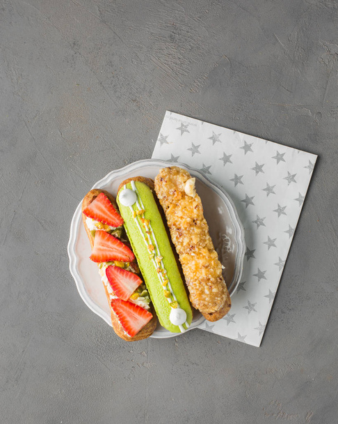 French choux pastry (eclairs) with fresh strawberries, vanilla cream, hazelnuts and pistachio macarons on white plate.Beautiful background with blank. Restaurant concept. Flat lay - Photo, image