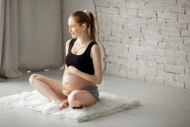 beautiful young pregnant girl engaged in gymnastics in the interior - Foto, Imagem
