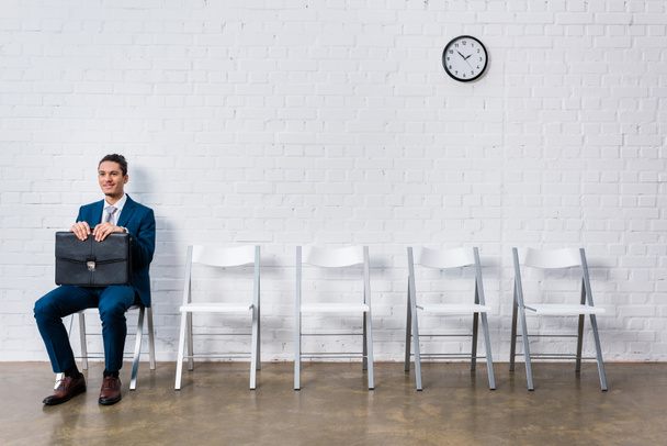 Smiling man with briefcase waiting for interview while sitting on chair - Photo, Image