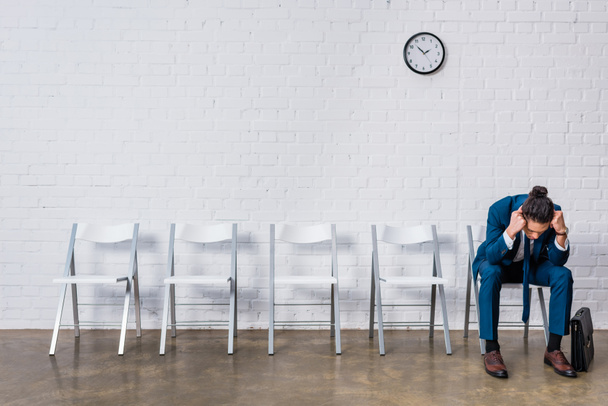 Наголошений бізнесмен сидить на стільці і чекає на співбесіду
 - Фото, зображення