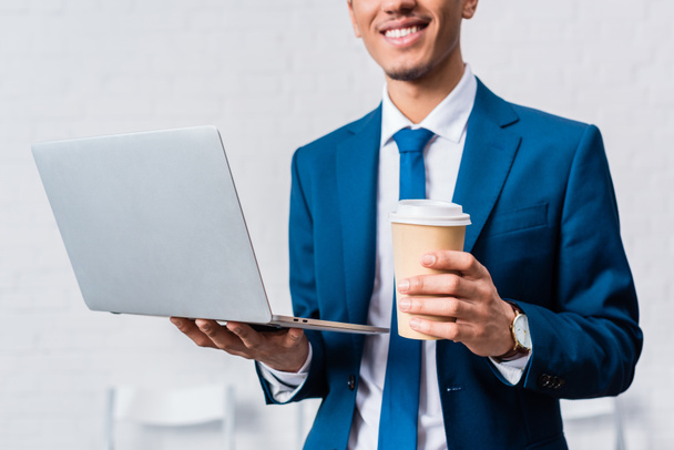 African american businessman holding laptop and coffee cup - Фото, зображення