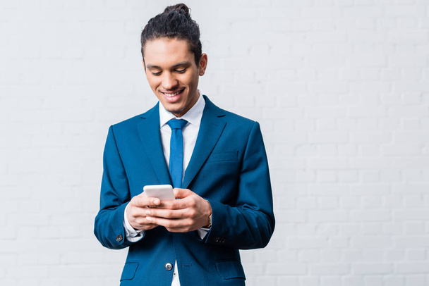 African american businessman using smartphone on white wall background - 写真・画像