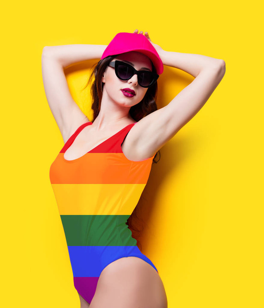 Elegant brunette woman in pink swimsuit and fashion cap. Sexy lady in pink beachwear, sunglasses enjoying sun on yellow summer background - Photo, Image