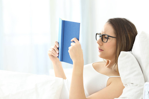 Woman reading a book wearing eyeglasses on the bed - Foto, Imagen