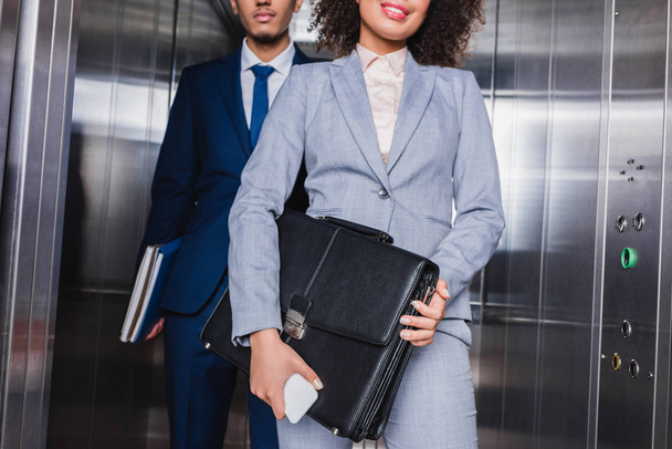 Vista recortada de mujer de negocios con maletín y hombre con carpetas de pie en ascensor
 - Foto, Imagen