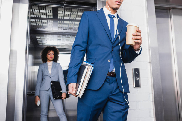 Zakenman in oortelefoons met koffiekopje wandelen van de lift met zakenvrouw - Foto, afbeelding