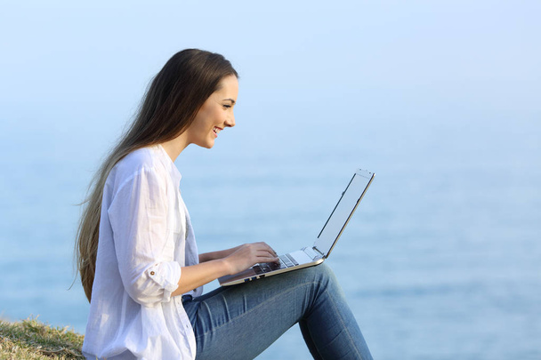 Woman using a laptop on the grass on the beach - Foto, immagini