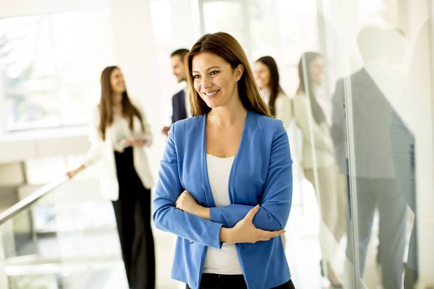Young businesswoman standing in the office and other young business  people talking in the background - Photo, Image