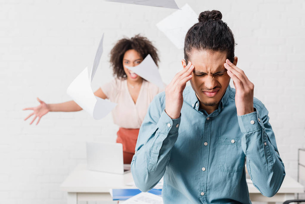 Businessman suffering from headache while his female colleague yelling in office - Foto, Imagen