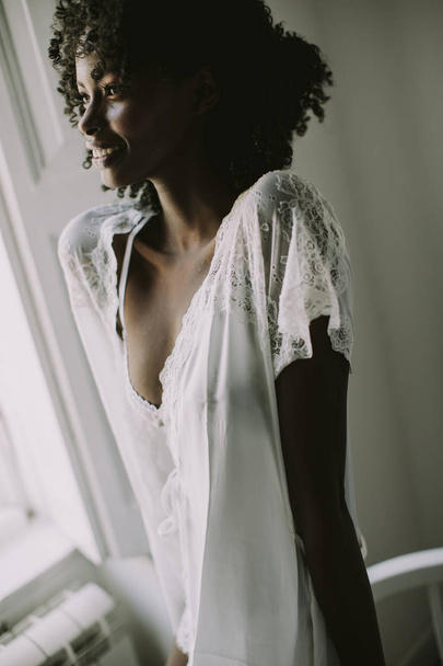 Kaunis nuori afrikkalainen amerikkalainen nainen poseeraa huoneessa ikkunan vieressä
 - Valokuva, kuva