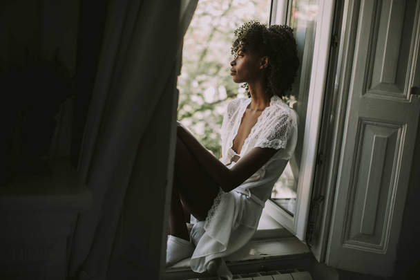 Красивая молодая черная женщина сидит на окне в комнате
 - Фото, изображение
