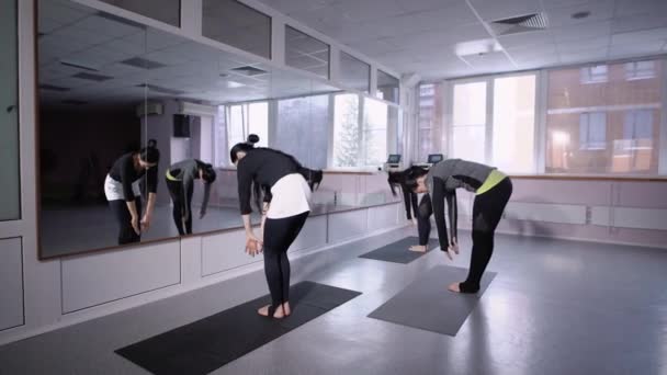 las mujeres jóvenes de una manera deportiva practican ejercicios de respiración y estiramiento en esteras de yoga frente a un espejo en un club de fitness
 - Metraje, vídeo