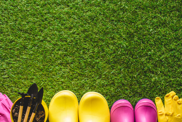 vista superior de botas de borracha, luvas de proteção e vaso de flores com ferramentas de jardinagem
  - Foto, Imagem