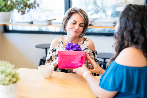 Melko keski-ikäinen nainen istuu kahvilassa ystävänsä kanssa ja vastaanottaa lahjan
 - Valokuva, kuva