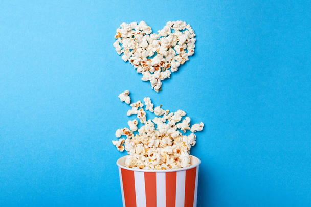 Me gusta ver películas. Palomitas de maíz derramadas en forma de cubo de corazón y papel en una tira roja sobre fondo azul
. - Foto, imagen