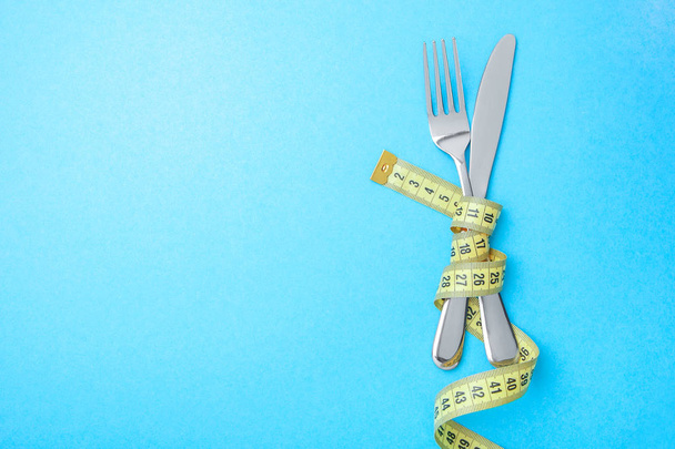 Diet menu in the restaurant or cafe. The fork and knife are wrapped in  yellow measuring tape on blue background. Copy space for text - Photo, Image