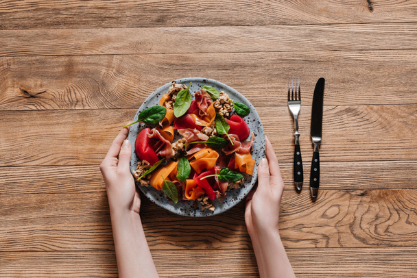 обрізаний знімок рук, що тримає тарілку з гастрономічним салатом з мідіями та овочами
 - Фото, зображення
