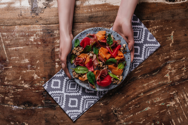 cropped shot of hands holding plate with salad with mussels, vegetables and jamon - Fotoğraf, Görsel