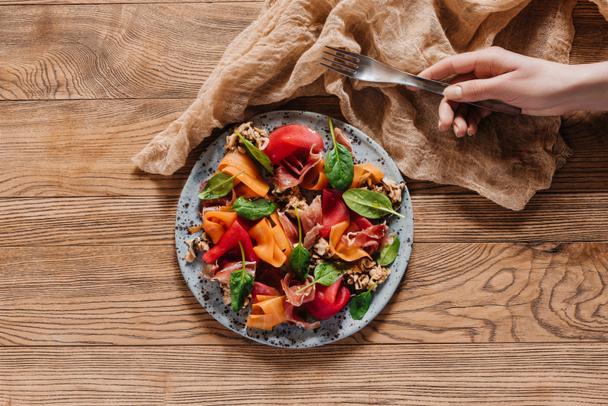 обрізаний знімок людської руки, що тримає виделку та салат з мідіями, овочами та джемоном на дерев'яному столі
 - Фото, зображення