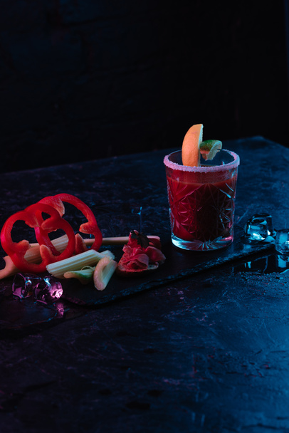 bloody mary cocktail in glass and vegetables with melting ice cubes on dark surface  - Foto, Imagem