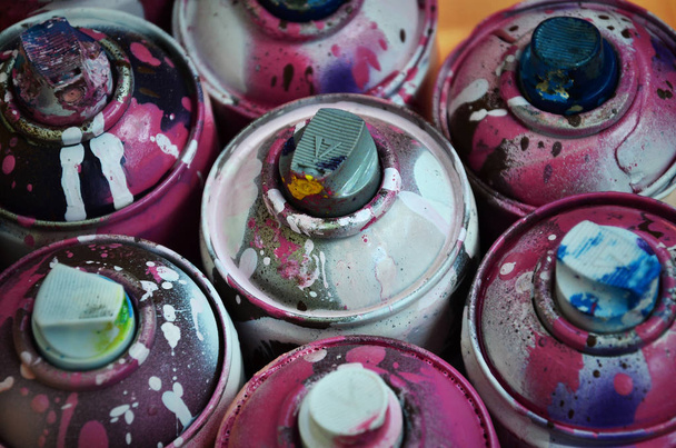 Stillleben mit einer großen Anzahl gebrauchter bunter Spraydosen mit Aerosolfarbe, die auf der behandelten Holzoberfläche in der Graffiti-Werkstatt des Künstlers liegen. verschmutzte und verschmutzte Dosen für Spraykunst - Foto, Bild