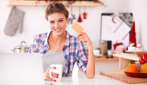 キッチンでコンピュータやクレジットカードを使用して笑顔の女性オンラインショッピング - 写真・画像