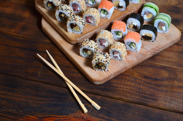 Um tiro detalhado de um conjunto de rolos de sushi japoneses e um dispositivo para seu uso (pauzinhos), que estão localizados em uma tábua de corte de madeira em uma mesa na cozinha de um bar de sushi
 - Foto, Imagem