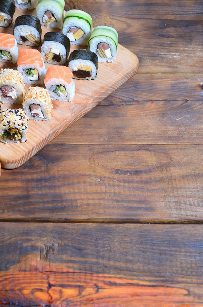 Σύνολο αριθμού ρολά σούσι βρίσκεται σε ένα ξύλινο κοπή του σκάφους σε ένα τραπέζι στην κουζίνα του σούσι μπαρ. Ένα παραδοσιακό πιάτο της ανατολίτικη κουζίνα - Φωτογραφία, εικόνα