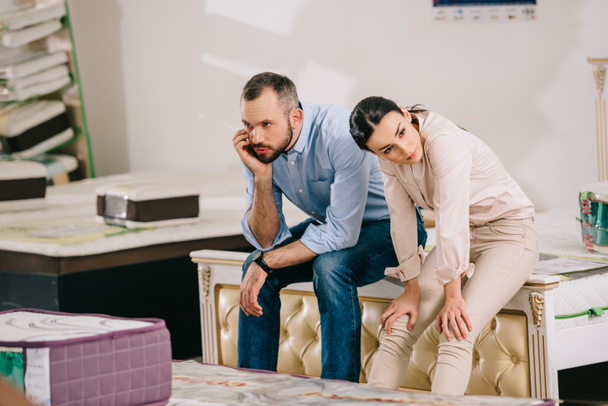 portrait of bored couple in furniture store with arranged mattresses - Photo, Image