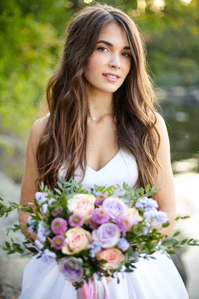 A beautiful bride with a bouquet of roses in her hands looks at the camera. Close-up. Outdoor - Photo, Image