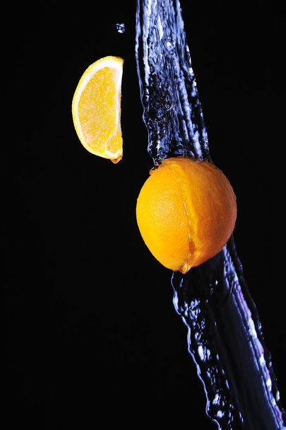 Orange with splash of water on a black background - Фото, изображение