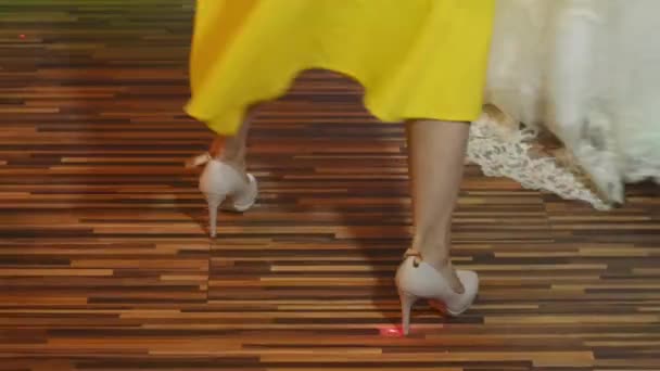 Twee vrouw dansen in de nachtclub, getoond in beweging met enige benen zichtbaar. Een meisje in een witte bruidsjurk, de tweede in een gele jurk en schoenen. - Video