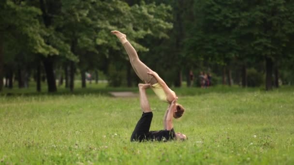 Beau couple pratiquant l'acro yoga. Jeunes instructeurs de yoga pratiquent dans un parc de la ville sur l'herbe verte. Deux jeunes qui réussissent effectuent des exercices d'acro yoga. Homme et une femme apprennent le yoga au coucher du soleil
. - Séquence, vidéo