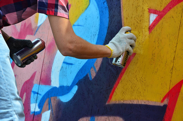 A hand with a spray can that draws a new graffiti on the wall. Photo of the process of drawing a graffiti on a wooden wall close-up. The concept of street art and illegal vandalism - Foto, afbeelding