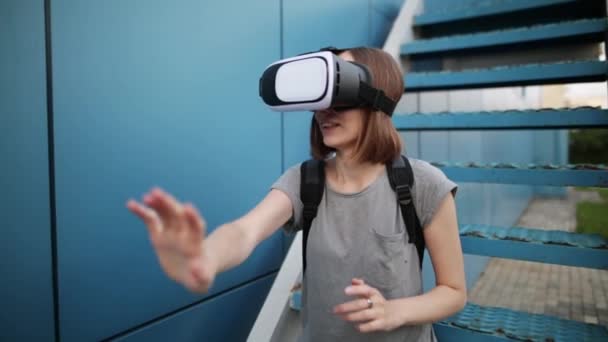 Zukunft ist jetzt. schöne junge Frau auf einer Treppe spielen Spiel in vr Brille. junge kaukasische Frau berührt etwas mit einer modernen Virtual-Reality-Brille auf blauem Hintergrund. - Filmmaterial, Video