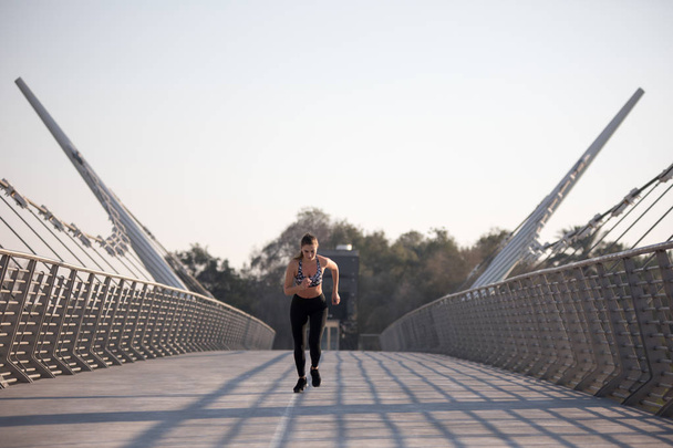 Active woman runner jogging across bridge, outdoors running, sport and healthy lifestyle concept. - Foto, imagen