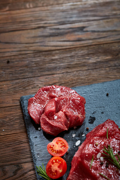 Composition of raw beefsteak on slate board with vegetables and seasoning, selective focus, close-up. - Fotoğraf, Görsel