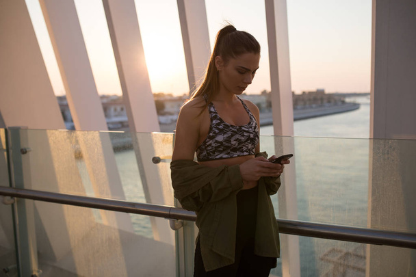 Chica atractiva utiliza un teléfono inteligente en el fondo de la puesta del sol
. - Foto, imagen
