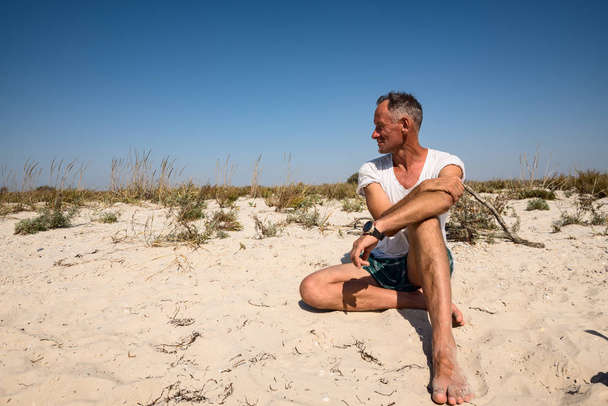 Smiling adventurer, as a modern savage, sits on the deserted sea - Фото, зображення