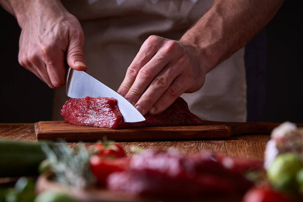 Strong professional mans hands cutting raw beefsteak, selective focus, close-up - Foto, Imagem