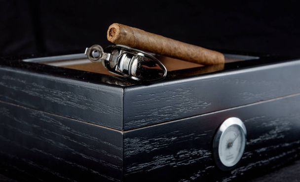 Багата запашна сигара на чорному х'юмідорі поруч з сигарним факелом. Чорний фон
 - Фото, зображення
