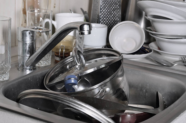 Величезна купа немитих посуду в кухонній мийці і на стільниці. Багато посуду та кухонної техніки перед пранням. Концепція повсякденної кулінарної рутини та складності
 - Фото, зображення