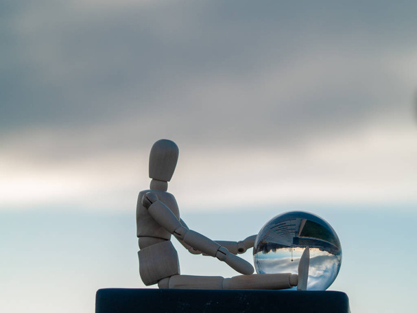 Wooden mannequin sitting with a crystal ball in his hands reflecting a landscape Ecology concept - Photo, Image