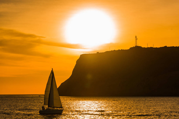 Zeilboot zeilen langs een landtong bij zonsondergang - Foto, afbeelding