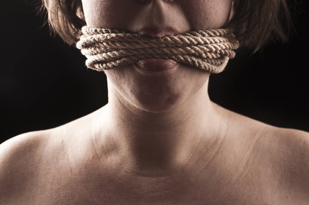 submissive girl gagged with rope on a black background - Photo, Image