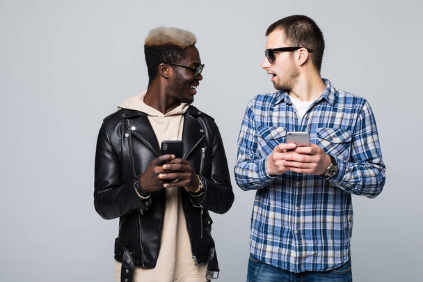 Dos amigos de raza mixta con adicción al teléfono se miran aislados sobre un fondo gris. Amistad multirracial
 - Foto, Imagen