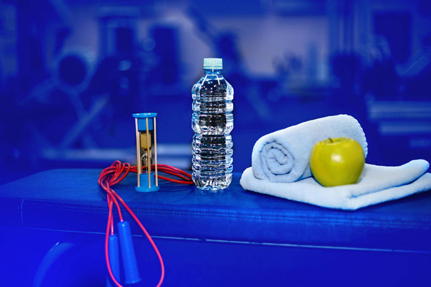 fitness room, pause between training, a bottle of water with a towel and a green apple, a skipping rope, toned - Photo, Image