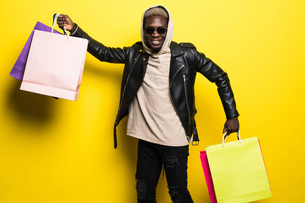 Hombre afroamericano con coloridas bolsas de papel después de comprar aisladas sobre fondo amarillo
 - Foto, Imagen