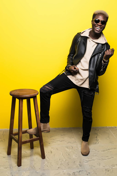 Portrait of a happy young afro american man listening to music with headphones and playing on invisible guitar isolated over yellow background - Photo, Image